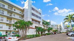 A multi-story hotel with balconies, a parking lot, and palm trees.