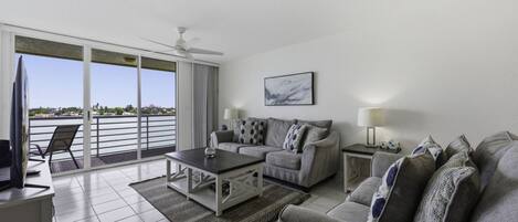 Una sala de estar con sofá, una mesa de centro, televisor y balcón con vistas.
