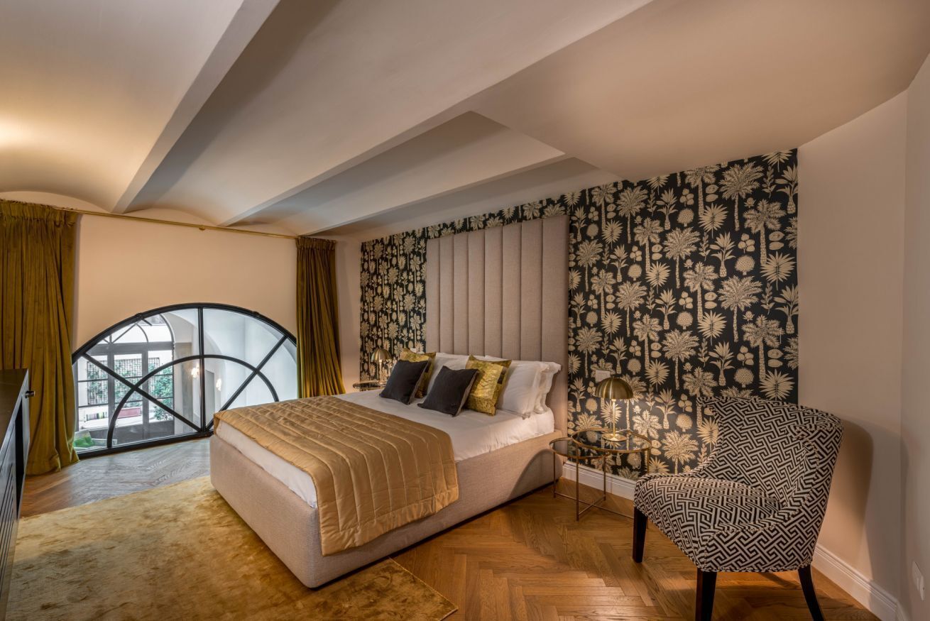 A bedroom with a bed, a chair, a window, and a patterned wall.