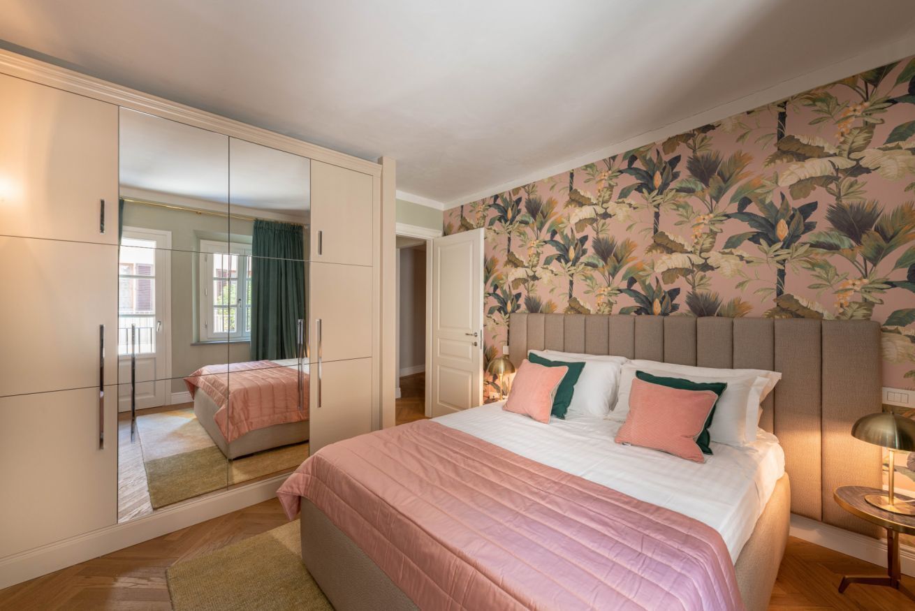 A bedroom with a large bed, a wardrobe with a mirror, and a floral wallpaper.