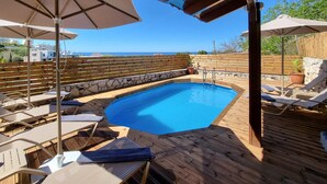A wooden deck with a swimming pool, lounge chairs, and umbrellas.