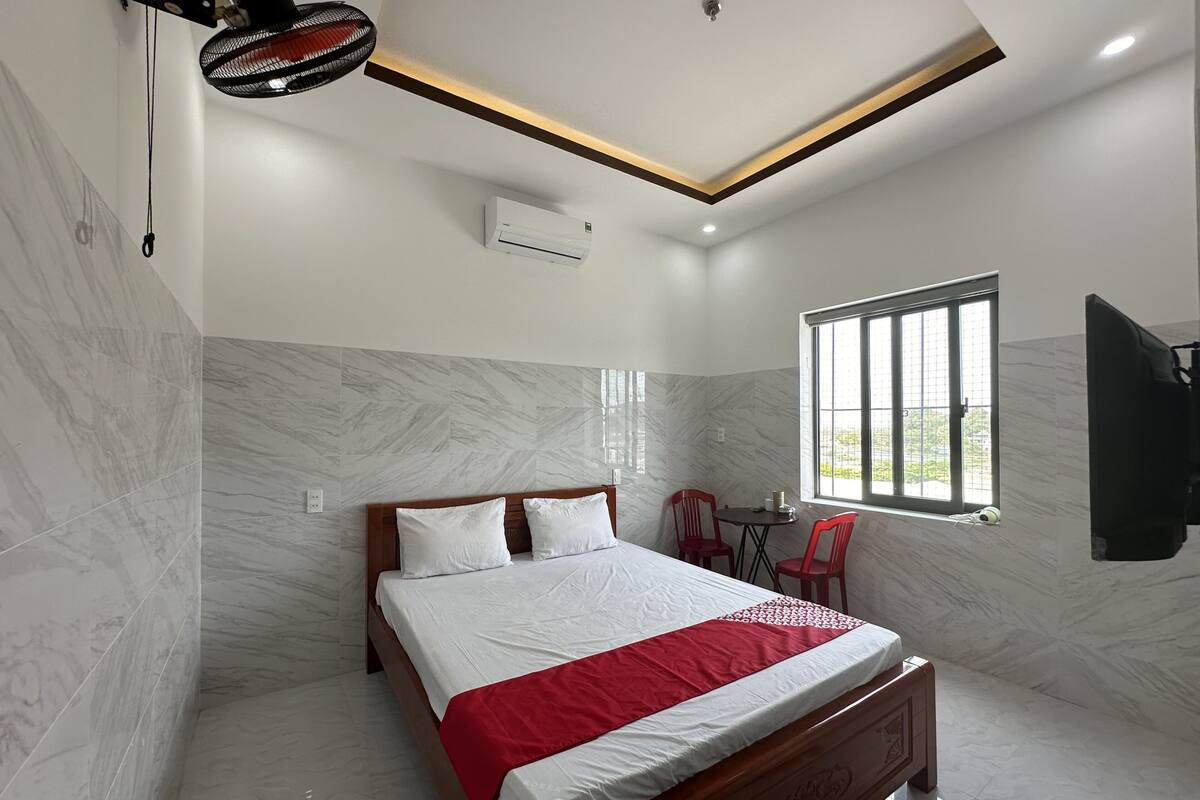 A bedroom with a bed, a ceiling fan, a window, and a TV.