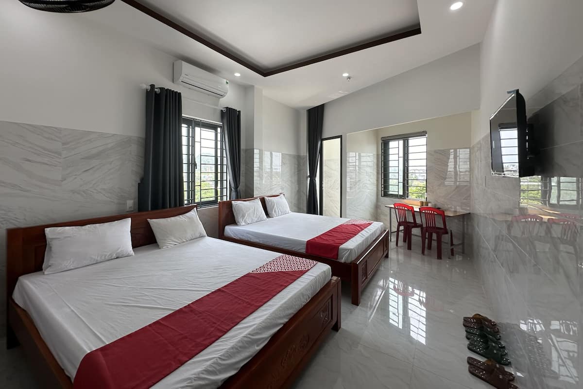 A hotel room with two beds, a desk, chairs, a TV, and a balcony with a view.