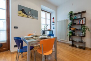 Uma área de refeições com uma mesa posta para dois, duas cadeiras, uma estante de livros e um quadro na parede.