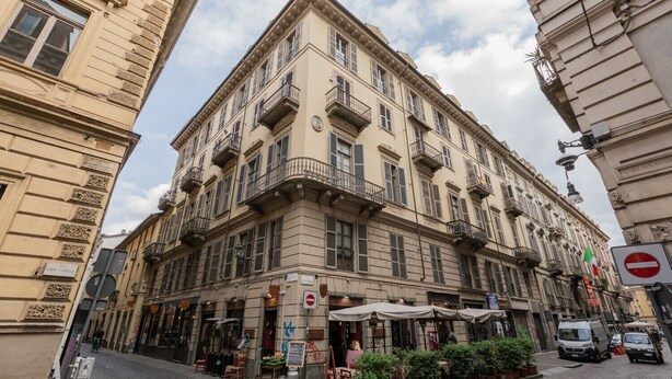 A historic building with multiple balconies, a ground-level café, and a cobblestone street. - La Corte by Wonderful Italy (Torino)