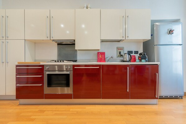 A modern kitchen with stainless steel appliances, a red and white cabinet design, and a wooden floor.