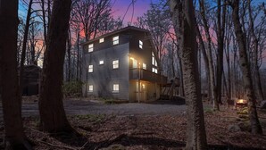 A modern two-story building with multiple windows, surrounded by trees and a gravel driveway. - Spacious and Remodeled Cabin in Poconos Mountain Resort. Hot Tub and Game Room! (Clifton Township)