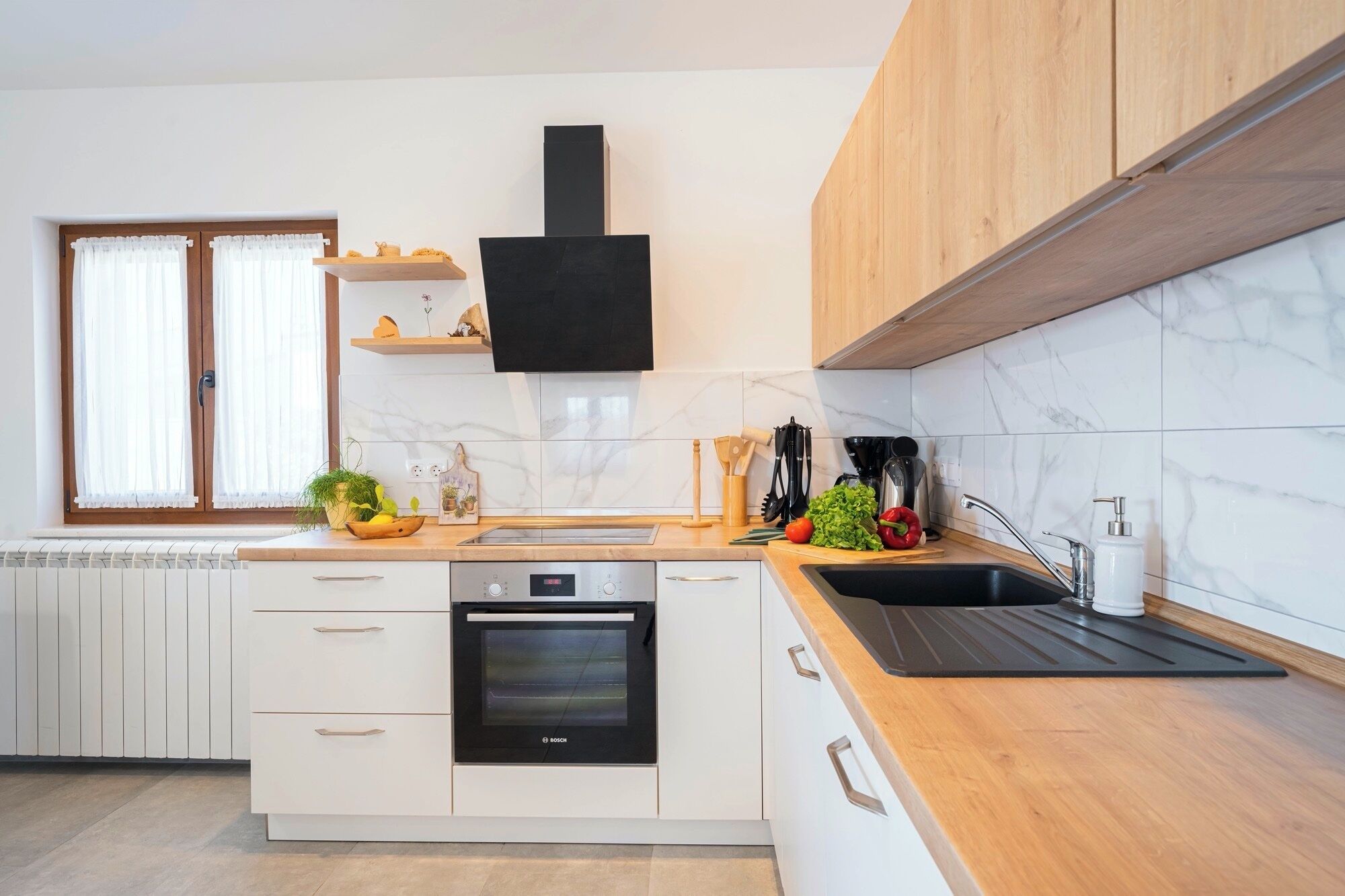 Una cocina moderna con armarios blancos, un horno Bosch, una campana extractora negra y una encimera de madera.