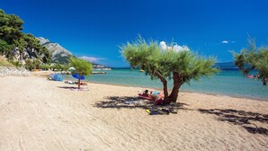 A beach with clear blue water, a few trees, and people relaxing. - Villa Flower with 3 en-suite bedrooms, heated pool, sea views (Jesenice)