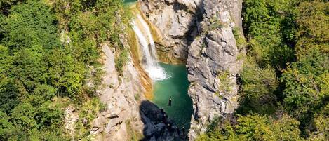 Vista aérea de una formación rocosa natural con una cascada y una poza de agua en su base.