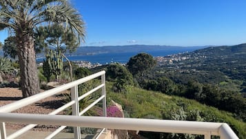 Un balcon doté d’une balustrade, offrant une vue sur le paysage urbain côtier, notamment sur la mer et les collines lointaines.