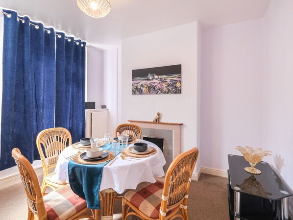 A dining room with a table set for four, a fireplace, and a painting on the wall.
