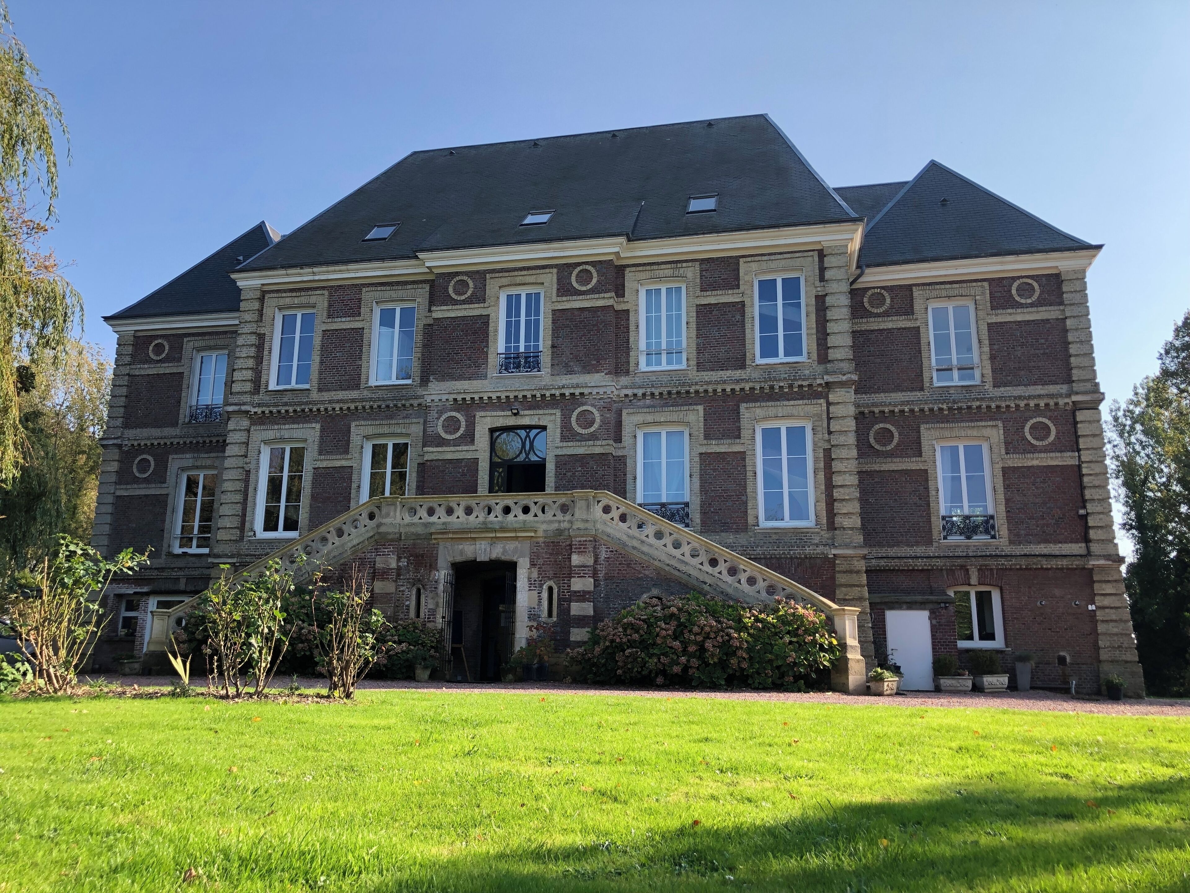 Un grand bâtiment historique à la façade symétrique, doté de nombreuses fenêtres et d’une entrée centrale avec un escalier.