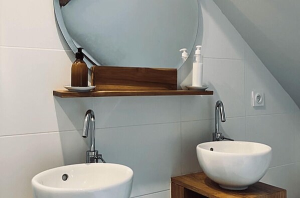 Un baño con dos lavamanos, un estante de madera con artículos de aseo y un espejo grande.