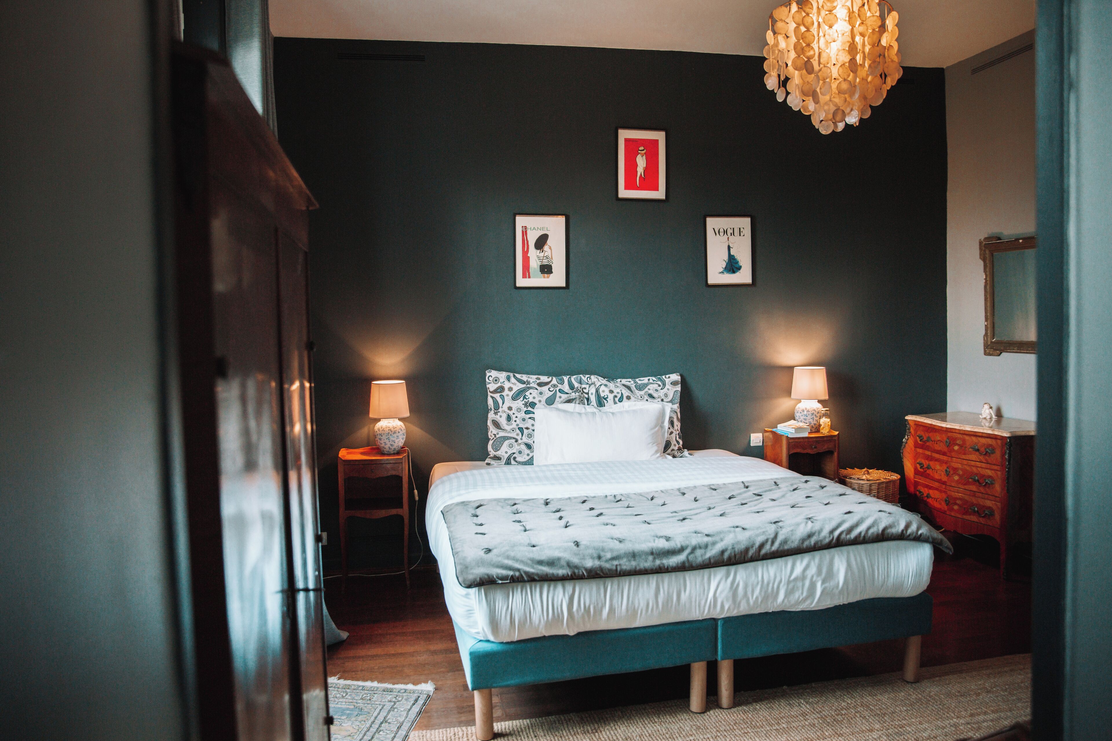 Un dormitorio con una cama grande, dos mesitas de noche con lámparas, un aparador y cuadros en la pared.