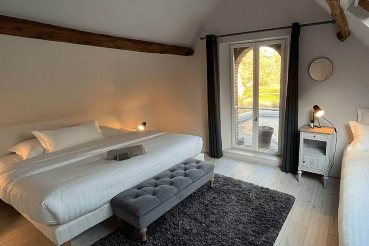 Ein Schlafzimmer mit einem großen Bett, einer Bank, einem Nachttisch und einem Fenster mit Vorhängen.