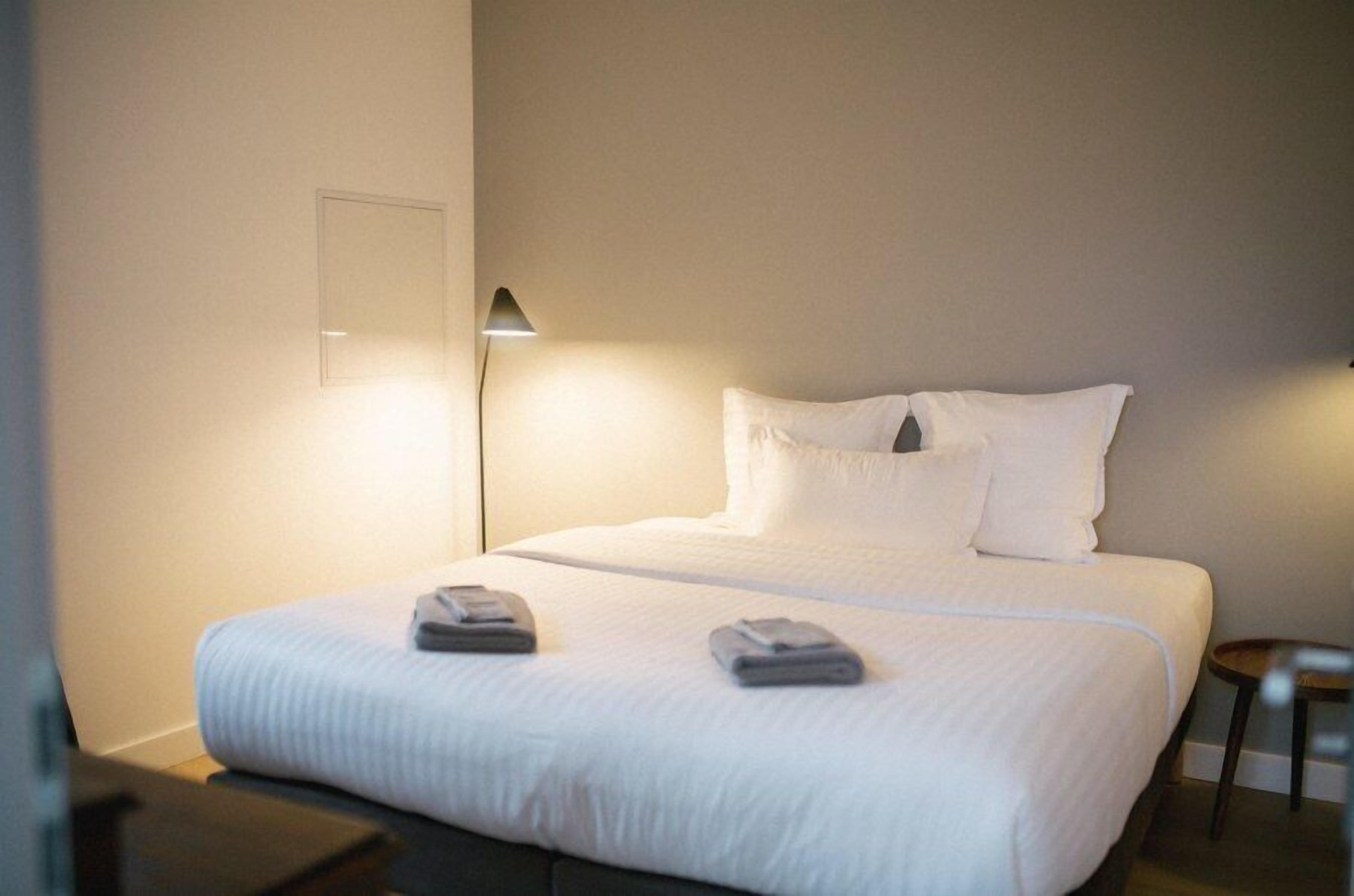 Una habitación de hotel con una cama bien hecha, una lámpara de noche y una mesita.