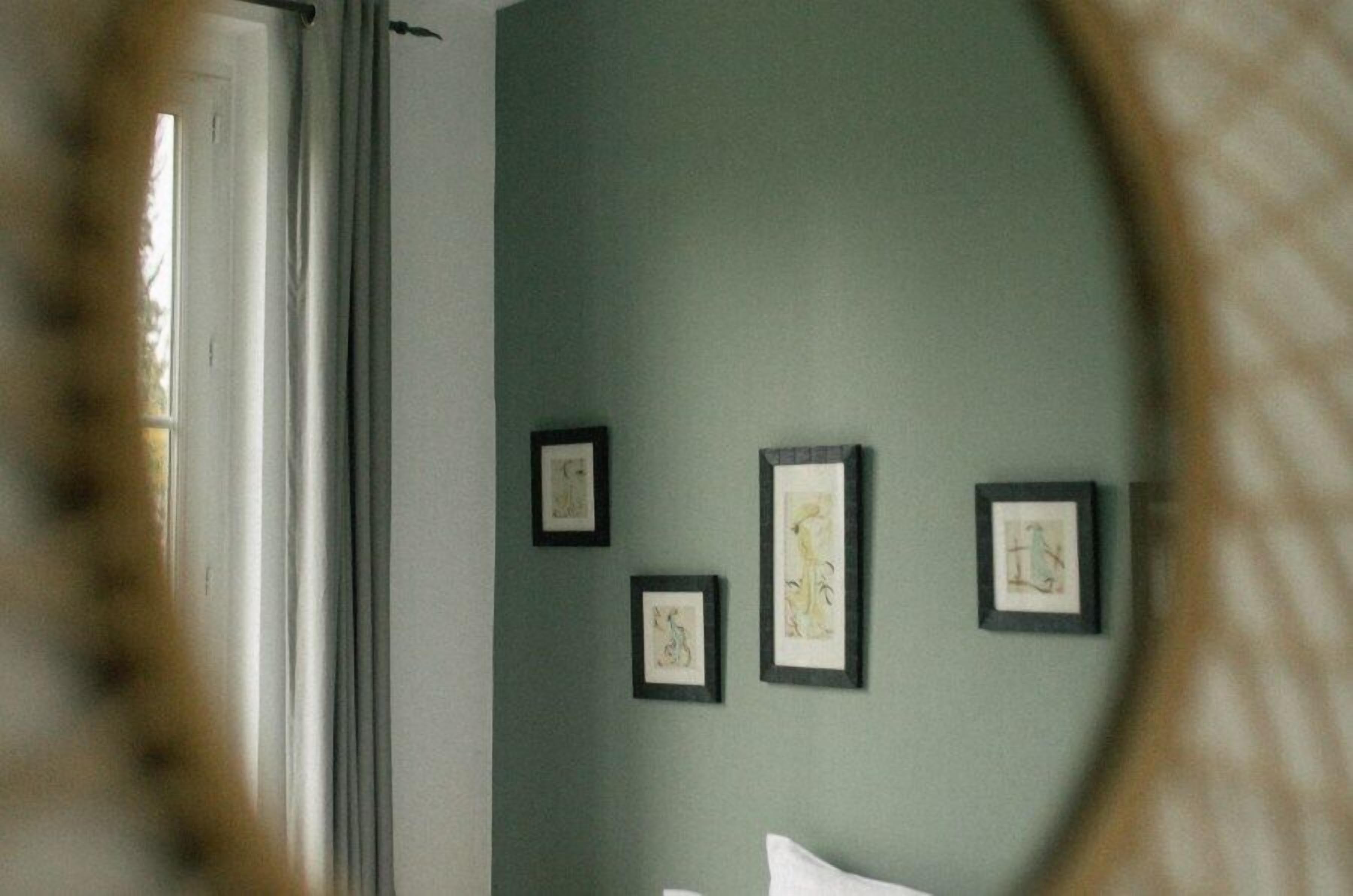 A room with a bed, a window with curtains, and three framed artworks on the wall.