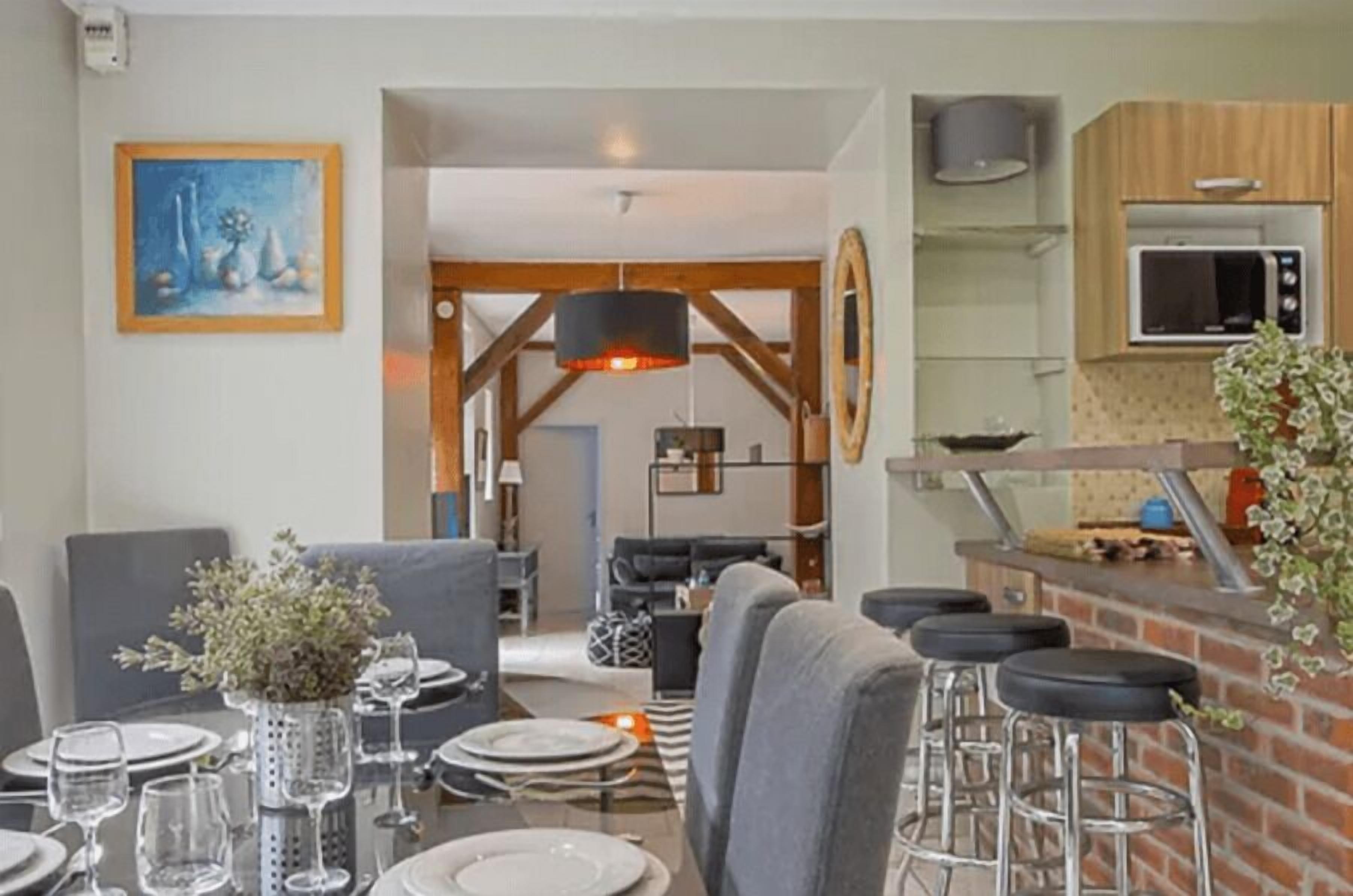 Un comedor con una mesa dispuesta para cuatro personas, una barra con taburetes, una cocina equipada con microondas y una sala de estar con sofá y televisor.