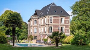 Un edificio grande e storico con piscina, circondato da rigogliosa vegetazione e palme.