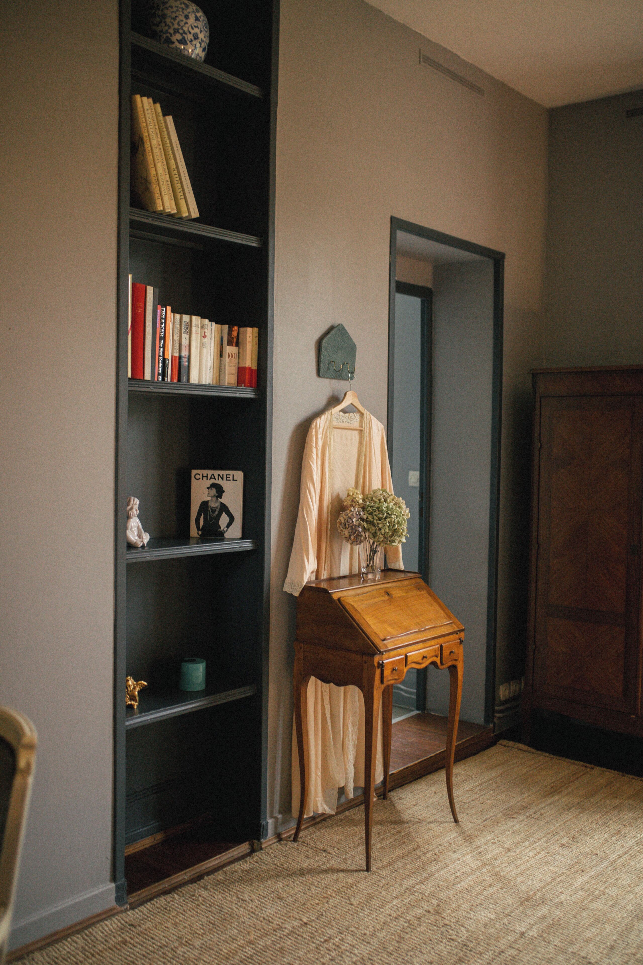 A room with a bookshelf, a wooden side table with a vase, and a mirror on the wall.
