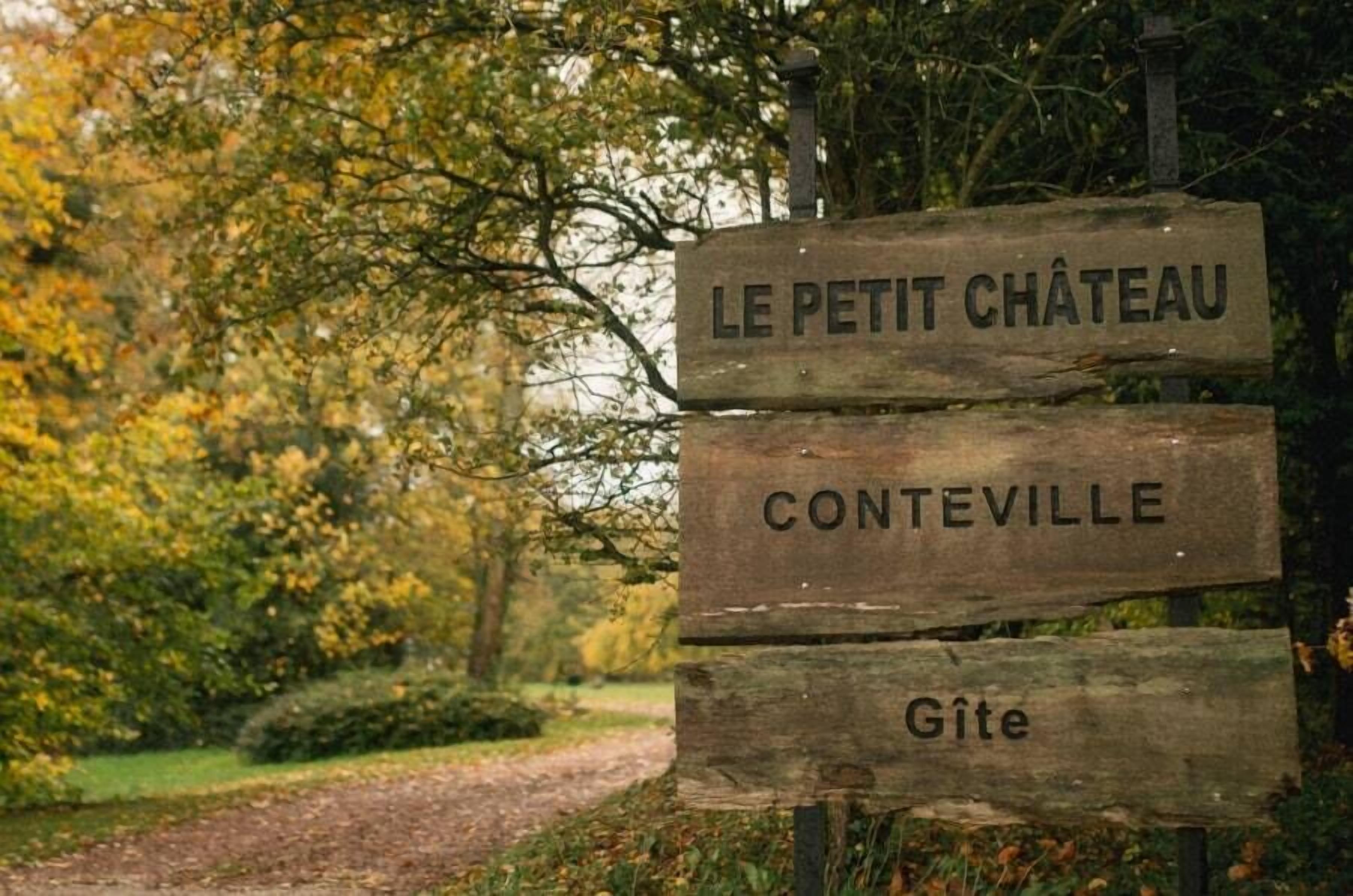 Un panneau indicateur en bois sur lequel on peut lire « LE PETIT CHÂTEAU » et « CONTEVILLE ».