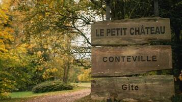 Un panneau indicateur en bois sur lequel on peut lire « LE PETIT CHÂTEAU » et « CONTEVILLE ».