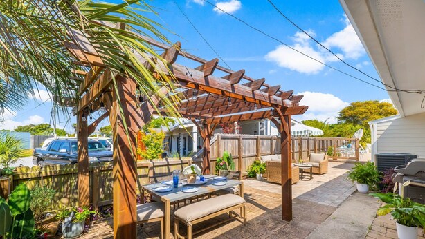 Une terrasse extérieure couverte, agrémentée d’une pergola en bois, d’une table à manger pour deux personnes et de divers pots de plantes.