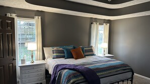 A bedroom with a bed, nightstands, a dresser, and a window with curtains.