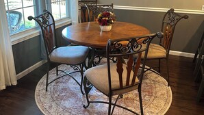 A dining area with a round wooden table, six chairs, a chandelier, and a decorative wall piece.