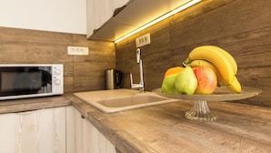 Een keuken met een magnetron, spoelbak en fruit op een glazen etagère.