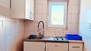 Een kleine keuken met een raam, een spoelbak en kastjes.
