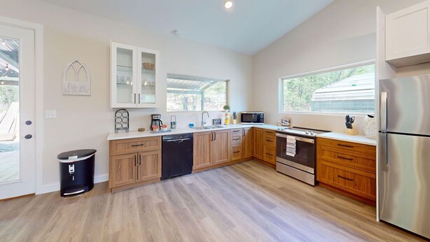 A modern kitchen with wooden cabinets, stainless steel appliances, and a black trash bin.