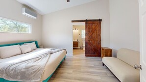 A bedroom with a bed, a sofa, a wooden door, and a bathroom in the background.