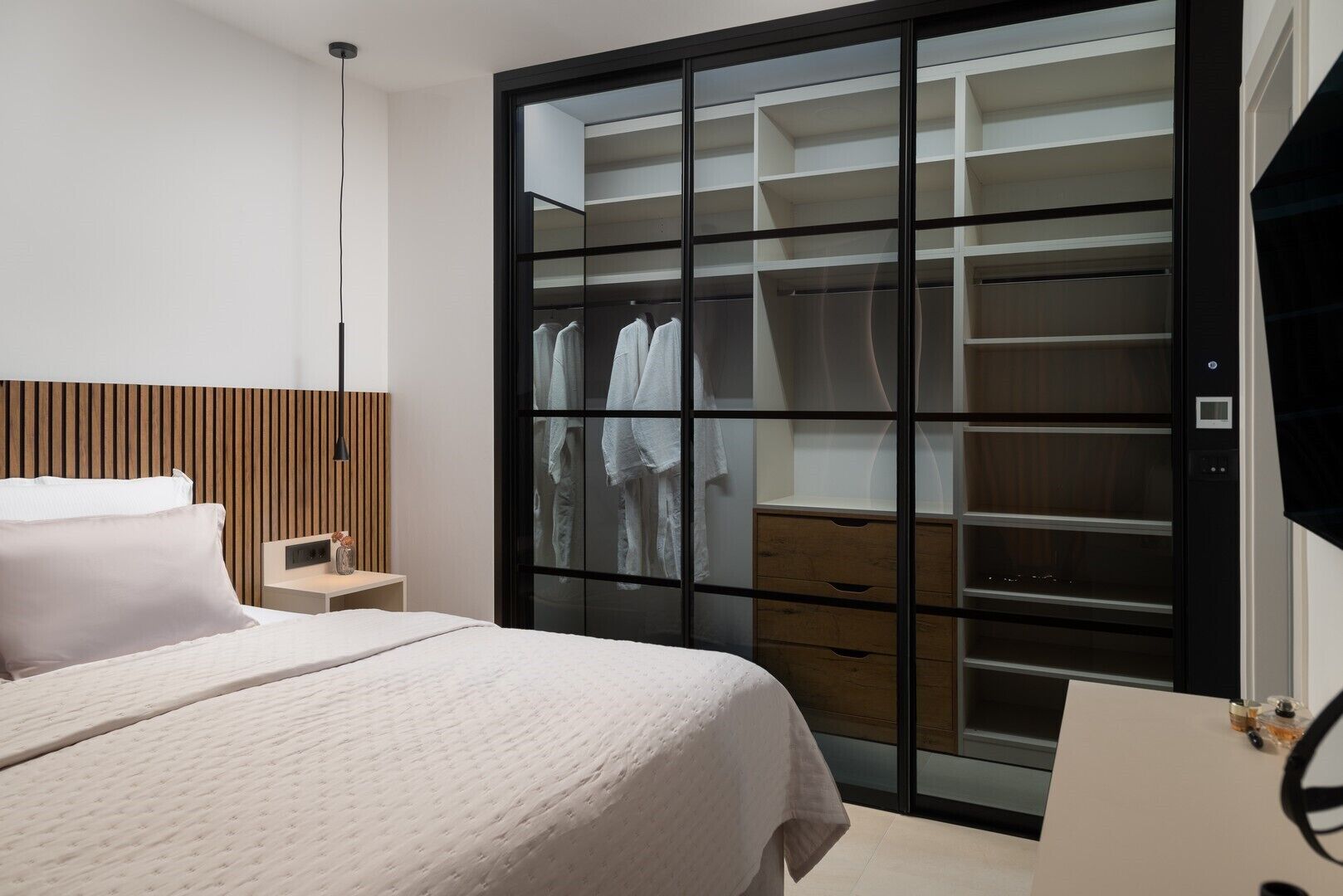 Un dormitorio con cama, mesita de noche, armario con espejo y televisor.