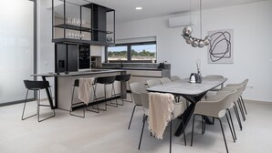 A modern kitchen with a dining area, featuring a large island, black chairs, and a view of the outdoors. - New Villa 55-Vrsi heated pool jacuzzi sauna bbq sea view (Vrsi)