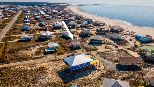 An aerial view of a coastal residential area with houses, some elevated on stilts, and a beach in the background. - Gulf Beachside 2 Bedroom, 1 Bath, Pet Friendly, Adorable! (Dauphin Island)