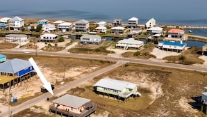 An aerial view of a coastal residential area with houses on stilts, a main road, and a body of water in the background. - Gulf Beachside 2 Bedroom, 1 Bath, Pet Friendly, Adorable! (Dauphin Island)
