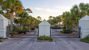A gated entrance with "Desolate Valley" signage, surrounded by palm trees and a gravel driveway. - Another Happy Clam, Beachside, 4/2, community POOL, dog friendly, sleeps 10 (Dauphin Island)