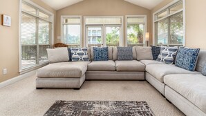 A living room with a sectional sofa, large windows with blinds, and a ceiling fan. - Another Happy Clam, Beachside, 4/2, community POOL, dog friendly, sleeps 10 (Dauphin Island)