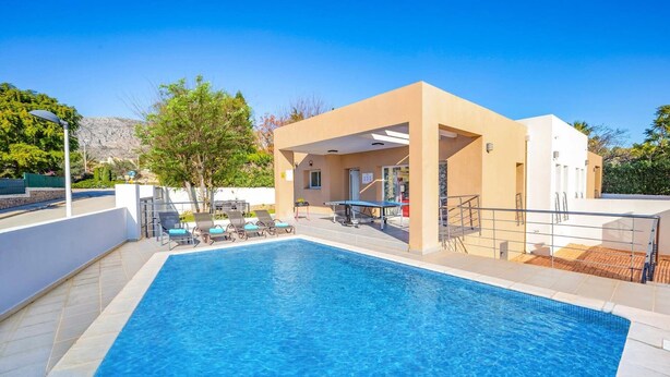 A swimming pool with lounge chairs and a sunbed, surrounded by a modern building with a flat roof and a small deck area. - Villa Pomera Dos by Villa Plus (Beniarbeig)