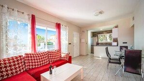 A modern living room with a red sofa, a white coffee table, and a dining area with a black chair and a glass table. - Villa Pomera Dos by Villa Plus (Beniarbeig)