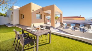 A modern outdoor patio with a dining table set for four, surrounded by chairs, and a pool area with lounge chairs. - Villa Pomera Dos by Villa Plus (Beniarbeig)