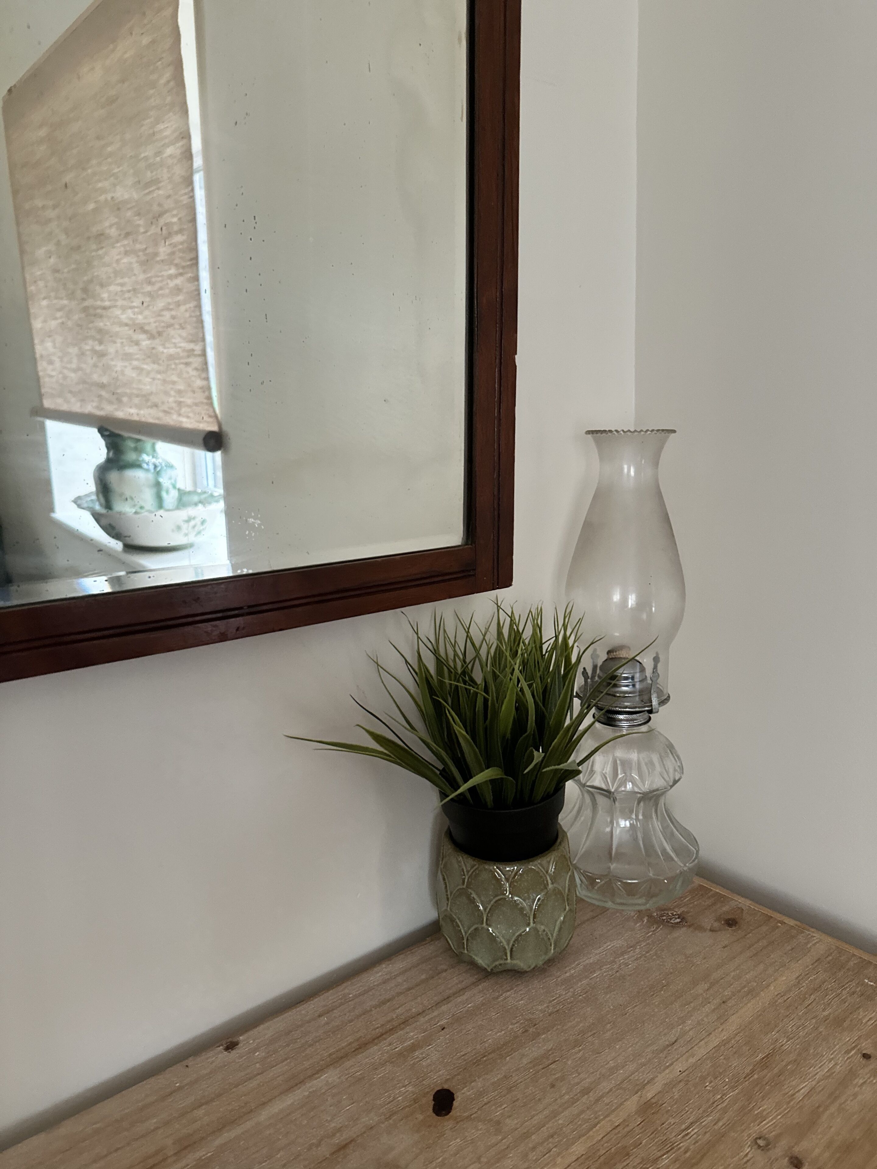 Une petite table d’appoint en bois, sur laquelle sont posés un pot de fleurs et un vase en verre transparent.