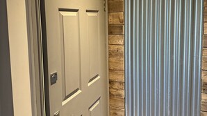 Una puerta con un letrero que indica un baño, un panel de pared de madera y una cortina de metal.