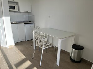 A small, white kitchen with a table and chairs, a microwave, and a trash can. - Studio "Giovanna" avec piscine & vue sur la baie d'Ajaccio ! (Alata)