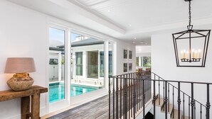 Un espacio interior amplio con vistas a una piscina exterior, un banco de madera con una lámpara y una escalera con barandilla de hierro forjado.