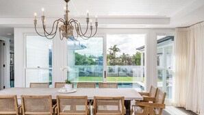 Un comedor amplio con una mesa grande y sillas de mimbre, una araña y ventanas grandes que ofrecen vistas a un jardín trasero.