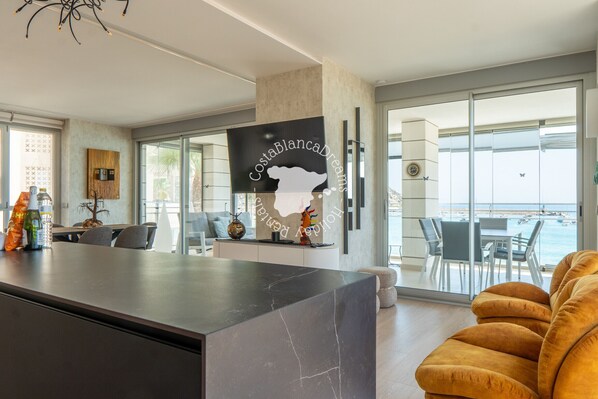 Une cuisine moderne avec un îlot en marbre, un coin repas offrant une vue sur la mer et un espace salon confortable avec un canapé.