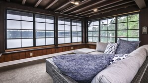 Ein gemütliches Zimmer mit einem großen Bett, einer Bank und Blick auf einen See durch große Fenster.